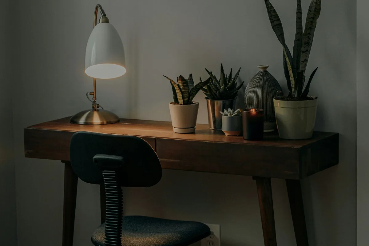Bàn làm việc gỗ đặt cạnh cửa sổ lớn của studio, đèn bàn và ghế tựa lưng
