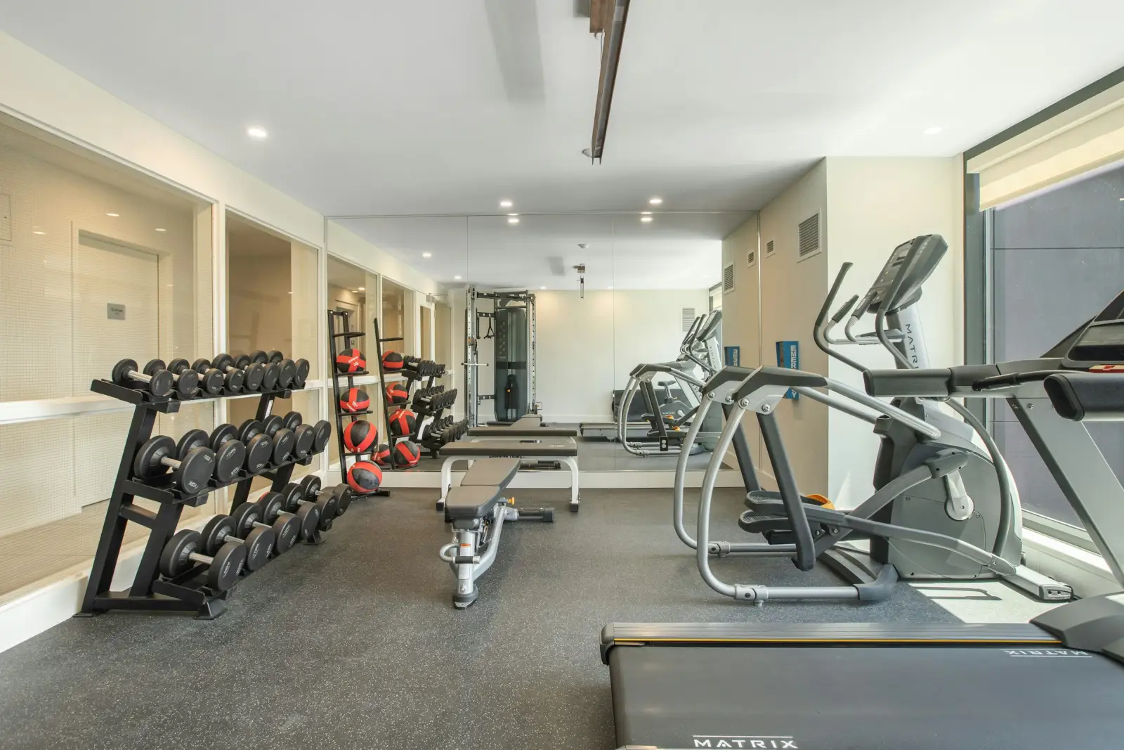 Phòng gym tầng trệt có máy chạy bộ, xe đạp tập và giá tạ, cửa kính nhìn ra sân vườn